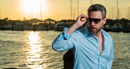 Portrait of handsome confident stylish man in yacht. Yacht club. Sexy man in fashion shirt posing on near yacht. Successful male model in the urban. Caucasian middle aged man near luxury yacht.の写真素材