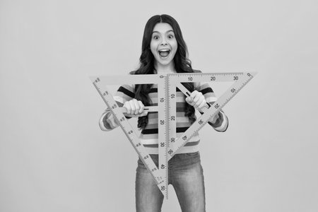 Amazed teenager. Measuring school equipment. Schoolgirl holding measure for geometry lesson, isolated on yellow background. Student study math. Excited teen girl.の写真素材
