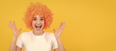 extremely happy funny girl with fancy look wearing orange hair wig on yellow background, happiness. Woman isolated face portrait, banner with copy space.の写真素材