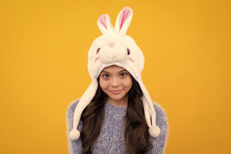 Bunny winter hat. Beautiful teen girl in a winter hat and a warm sweater. A child on a yellow...