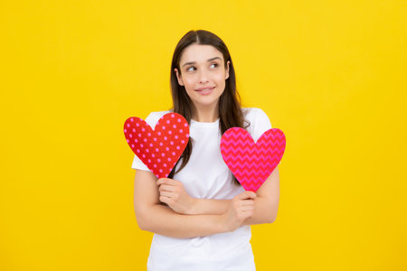 Girl feeling love. Young woman valentines day concept, girl with heart shaped card. Lovely charming girl holding in hands heart love symbol isolated on yellow background.の写真素材
