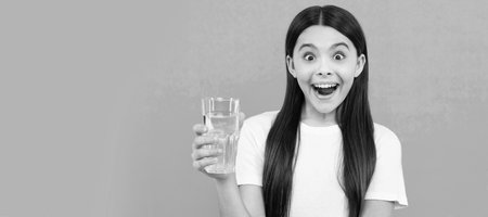surprised girl drink glass of water to stay hydrated and keep daily water balance, drink water. Banner of child girl with glass of water, studio portrait with copy space.の写真素材