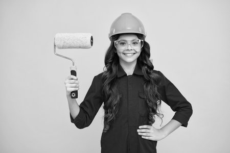 Painter in workshop. Renovation and repair. Teen girl in helmet with painting brush. Child in hard hat. Kid builder painter on construction site. Happy positive and smiling emotions of teenager girl.の写真素材