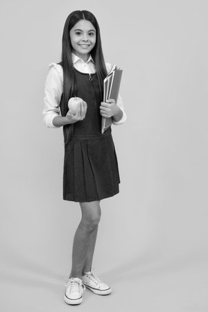 Full length of schoolchild, teenage student girl with school bag backpack hold aplle on yellow isolated studio background. Children school and education concept.の写真素材