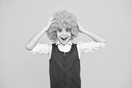 Funny kid in curly redhead wig. Time to have fun. Teen girl with orange hair, being a clown. Excited face, cheerful emotions of teenager girl.の写真素材
