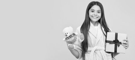 Teenager birthday. happy teen girl in home terry bathrobe with toy and present box, discount. Kid girl with gift, horizontal poster. Banner header with copy space.の写真素材