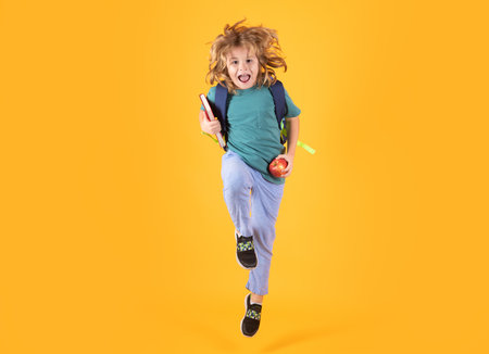 Photo of excited little school jumping holding book, empty space isolated yellow background. Amazed school child jump with backpack. Learning and knowledge. Go study. Education concept. Run and jump.の写真素材