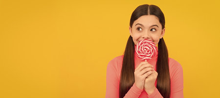 dreamy kid with lollipop candy on stick on yellow background, caramel. Teenager child with sweets, poster banner header, copy space.の写真素材