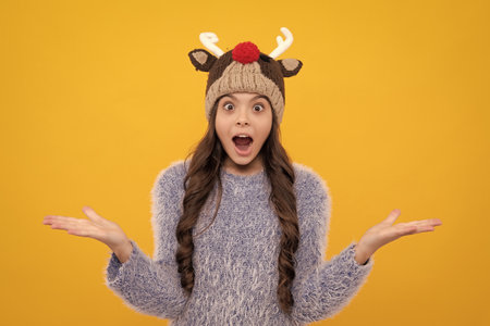 Beautiful teen girl in a winter hat and a warm sweater. A child on a yellow isolated background. Excited face, cheerful emotions of teenager girl.の写真素材