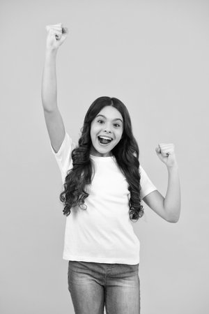 Amazed teenager. Excited teen girl. Teenager child overjoyed successful do winner gesture clench fist say yes isolated on yellow background studio.の写真素材