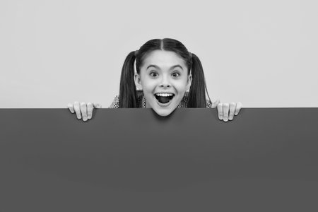 Teenage girl holds a blank for notification informing. Advertisement and sale. Markets and shops sales concept, blank board for copy space. Happy positive and smiling emotions of teen girl.の写真素材