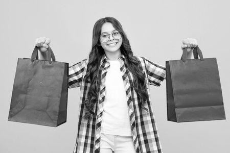 Funny teen girl hold shopping bag enjoying sale isolated on yellow. Portrait of teenager schoolgirl is ready to go shopping.の写真素材