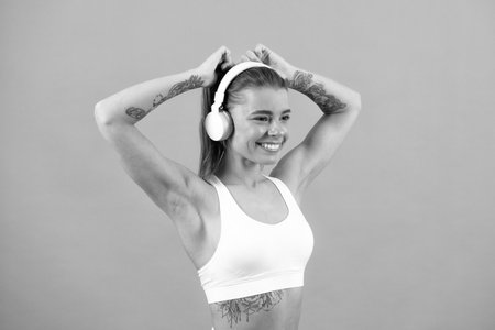 Young fitness woman runner with headphone posing on gray isolated background. Caucasian female athlete, muscular, sportive woman. Concept of youth healthy lifestyle.の写真素材