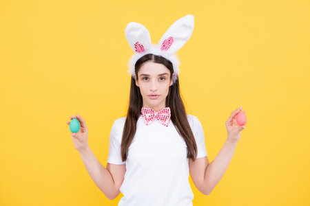 Easter eggs. Portrait of young girl with rabbit bunny ears isolated on yellow background. Easter...