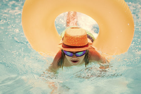 Child in swimming pool on inflatable ring. Kid swim with orange float. Water toy, healthy outdoor...