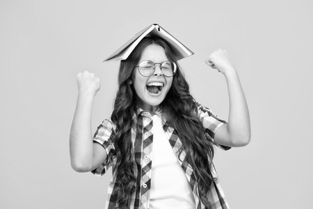 Amazed teen girl. Teen girl pupil hold books, notebooks, isolated on yellow background, copy space. Back to school, teenage lifestyle, education and knowledge. Excited expression, cheerful and glad.の写真素材