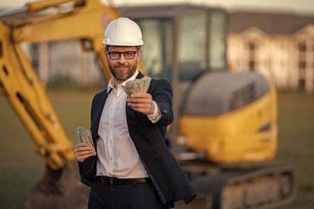 Buider man in suit and hardhat. Construction investor. Business man investor in front of construction site. Successful investor. Handsome man in suit and hardhat at building construction.の写真素材