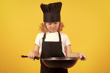 Little cook with cooking pan. Kid chef cook, studio portrait. Children cooking. Kid boy with apron and chef hat.の写真素材