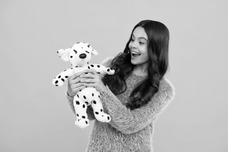 Teen girl in casual clothes hold soft toy for birthday on yellow background. Kid spending time with...