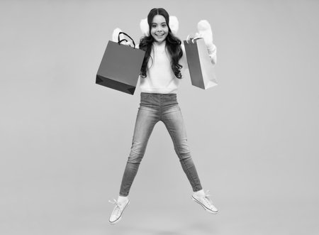 Girl teenager with shopping bags isolated on yellow backgound. Run and jump. Shopping and sale concept. Happy face, positive and smiling emotions of teenager girl.の写真素材
