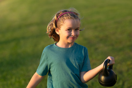 Child lifting the kettlebell in backyard outside. Kid raising a kettlebell. Cute child training with dumbbells. Kids fitness. Kid boy exercising with dumbbells. Healthy kids.の写真素材