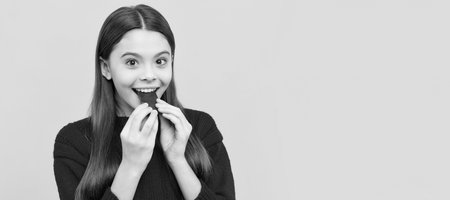 Happy girl child bite tasty chocolate slab yellow background, sweet-tooth. Horizontal poster of isolated child face, banner header, copy space.の写真素材