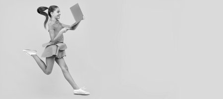 happy girl hurry up running using notebook to find sale and discount, copy space, shopping online. School girl portrait with laptop, horizontal poster. Banner header with copy space.の写真素材