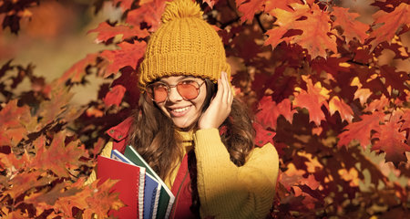 Autumn kid girl face in autumn fall leaves outdoor. positive child hold workbook on autumn leaves...