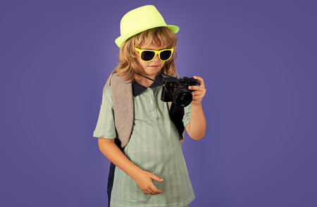 Child traveler with camera and backpack isolated on studio background. Tourist kid boy. Portrait of child travel with travel bag. Travel, adventure, vacation.の写真素材
