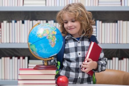 School boy looking at globe in library, geography lesson. School child student learning in class, study english language at school. Elementary school child. Portrait of funny pupil learning.の写真素材