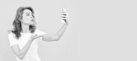 Gadget addicted. Selfie girl blogger yellow background. Woman give hand kissing to smartphone. Woman isolated face portrait, banner with mock up copy space.の写真素材