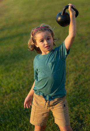 Child lifting the kettlebell in backyard outside. Sport activities at leisure with children. Sporty kid boy holding dumbbells kettlebell.の写真素材