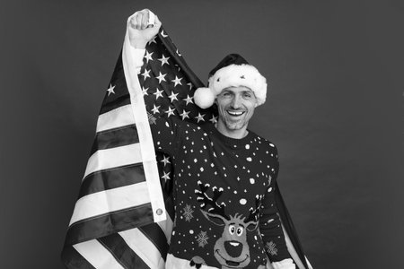 Santa hold american flag. Xmas in united states, usa. Man in Christmas santa hat, winter holiday, christmas background.の写真素材