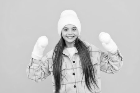 cheerful child in hat and mittens playing snowballs on yellow background, winter activityの写真素材