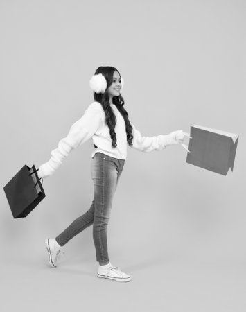 Funny teen girl hold shopping bag enjoying sale isolated on yellow. Portrait of teenager schoolgirl is ready to go shopping. Winter shopping sale.の写真素材
