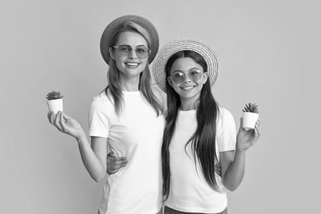 Happy mother and daughter teenager child girl with potted plant on yellow background. Cactus in pot.