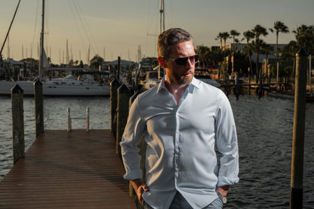 Portrait of handsome confident stylish man in yacht. Yacht club. Man in fashion shirt posing on near yacht. Successful male model in the urban. Caucasian middle aged man near luxury yacht.の写真素材