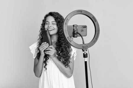 Teen girl hold hair conditioner or shampoo bottle in front of camera for vlog isolated on yellow...