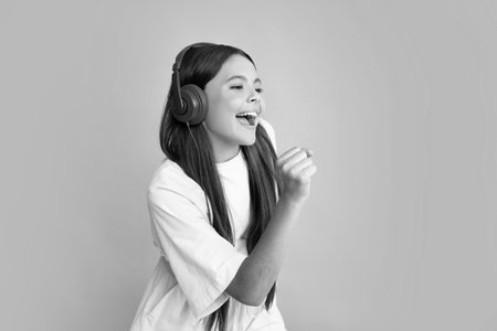 Child music concept. Teenager child girl dances in rhythm of melody, listens song in headphones. Child listening to music through earphones. Excited face, cheerful emotions of teenager girl.の写真素材