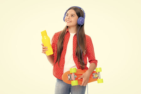 Teen girl 12, 13, 14 years old with skateboard and headphones over white studio background. Cool modern teenager in stylish clothes. Teenagers lifestyle, casual youth culture.の写真素材