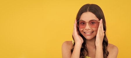 child with long hair in glasses. happy teen girl with curly hair on yellow background. Child face, horizontal poster, teenager girl isolated portrait, banner with copy space.の写真素材