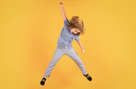 Funny boy jumping. Energetic kid boy jumping and raising hands up on isolated studio background. Full length body size photo of jumping high child boy, hurrying up running fast on yellow background.の写真素材
