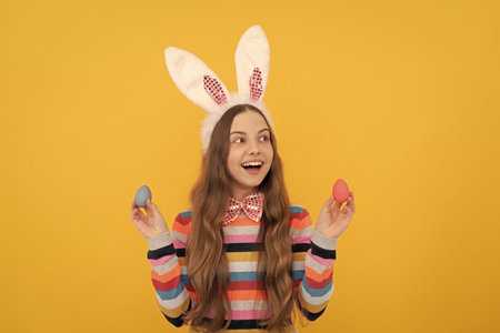 happy teen child in bunny ears and bow tie hold easter eggs on yellow backgroundの写真素材