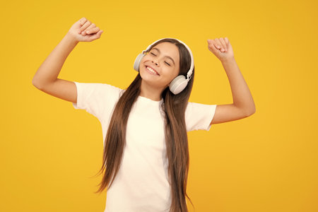 Teen girl in headphones listen to music. Wireless headset device accessory. Child enjoys the music in earphones on yellow background.の写真素材