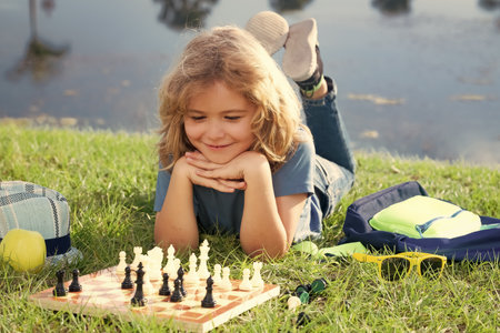 Concentrated child boy developing chess strategy, playing board game in backyard, laying on grass.の写真素材