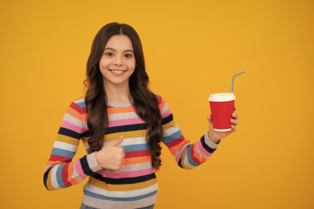 Child girl holding coffee cup. Coffee break and recess. Teenager hold plastic take away cup, drink cocoa, coffee or tea beverage. Happy teenager, positive and smiling emotions of teen girl.の写真素材