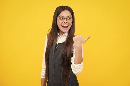Excited face, cheerful emotions of teenager girl. Portrait of cute teenager child girl pointing hand showing adverts with copy space over yellow background.の写真素材