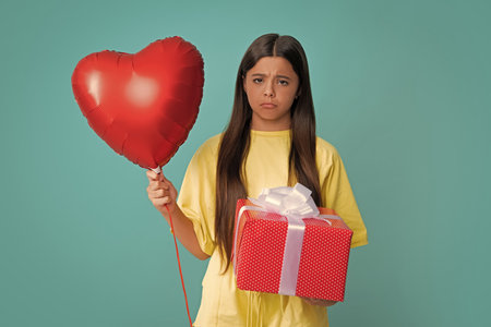 Angry teenager girl, upset and unhappy negative emotion. Teenager child with gift box. Present for holidays. Love valentines, heart balloon.の写真素材