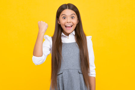 Excited face, cheerful emotions of teenager girl. Teenager child overjoyed successful do winner gesture clench fist say yes isolated on yellow background studio.の写真素材