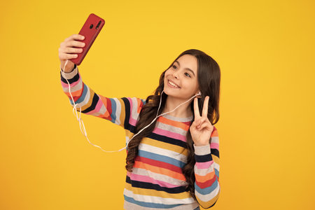 Kids selfie. Teenager child girl holding smartphone. Hipster girl with cell phone. Kid hold mobile phone texting in online social networks. Happy teenager, positive and smiling emotions of teen girl.の写真素材